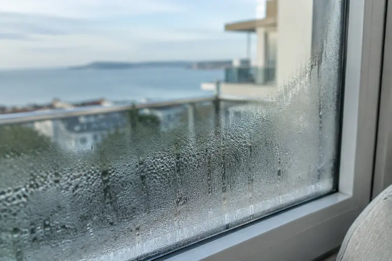 Gouttes de condensation perlant sur la vitre d'une fenêtre dans un appartement sur la Côte d'Azur.