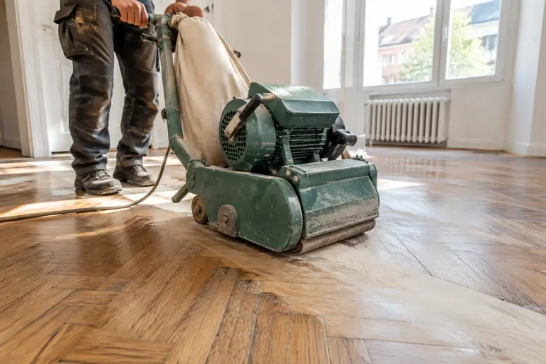 Artisan ponçant un parquet ancien d'appartement à Nice pour rénover la surface en bois