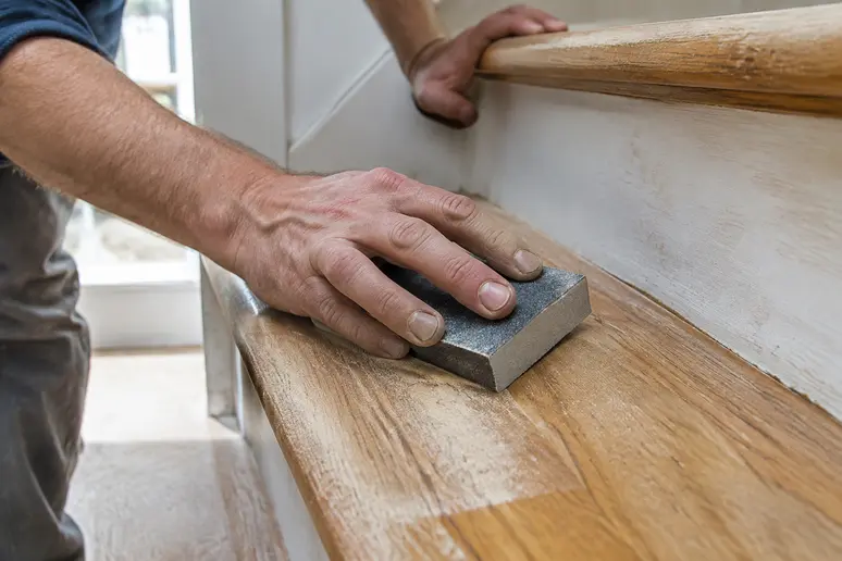 Ponçage manuel d'une marche d'escalier en bois avec un papier abrasif fin pour la peinture escalier bois