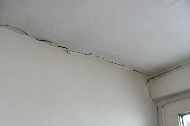 Fissure structurelle le long de la jonction entre le mur et le plafond bas d'un appartement niçois