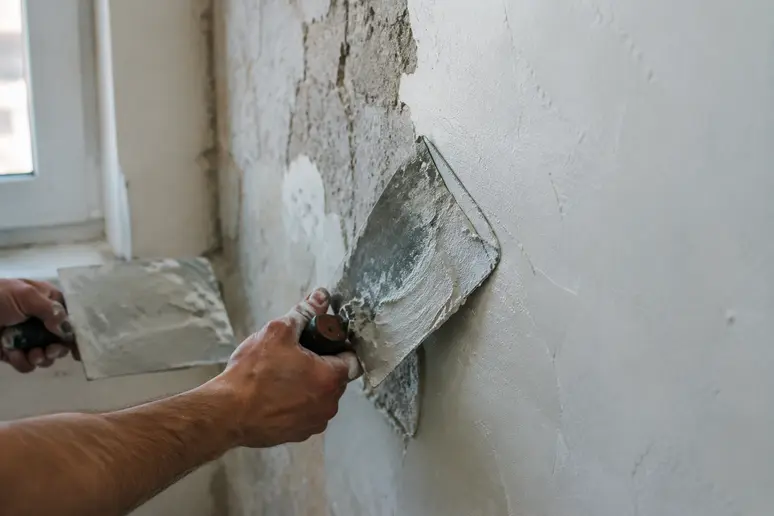 Application d'un enduit mur interieur à l'aide d'une spatule sur une surface abîmée.